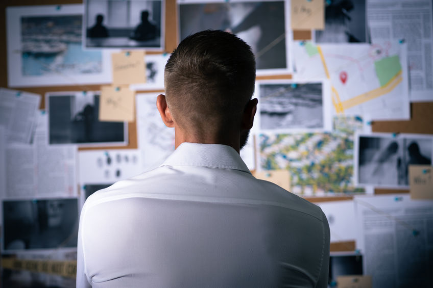 Private investigation services for a skip tracing case as the investigator looks at evidence posted on the wall.