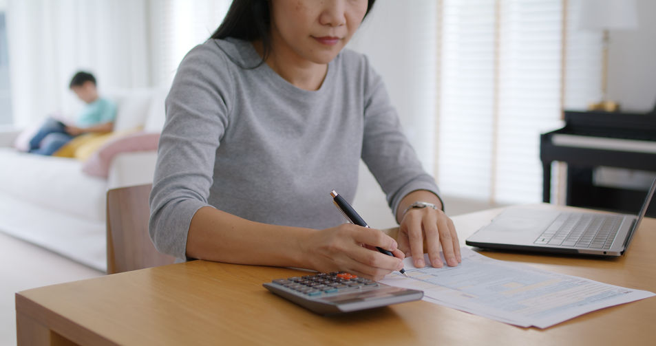 A woman calculating expenses while considering hiring private investigation services for a spousal support case.