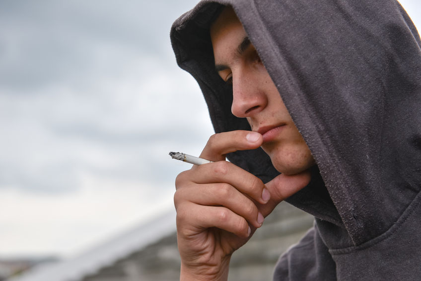 A teenager smoking a cigarette in heavy contemplation while his parents consider private investigation services to see if there is anything they should be concerned about.